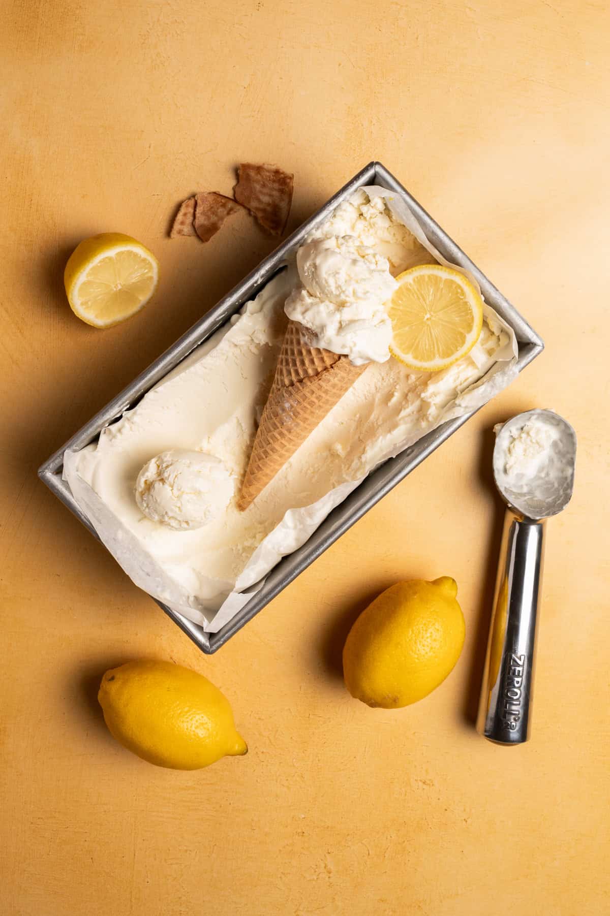 The no churn lemon ice cream is in a loaf pan with an ice cream scoop next to it.