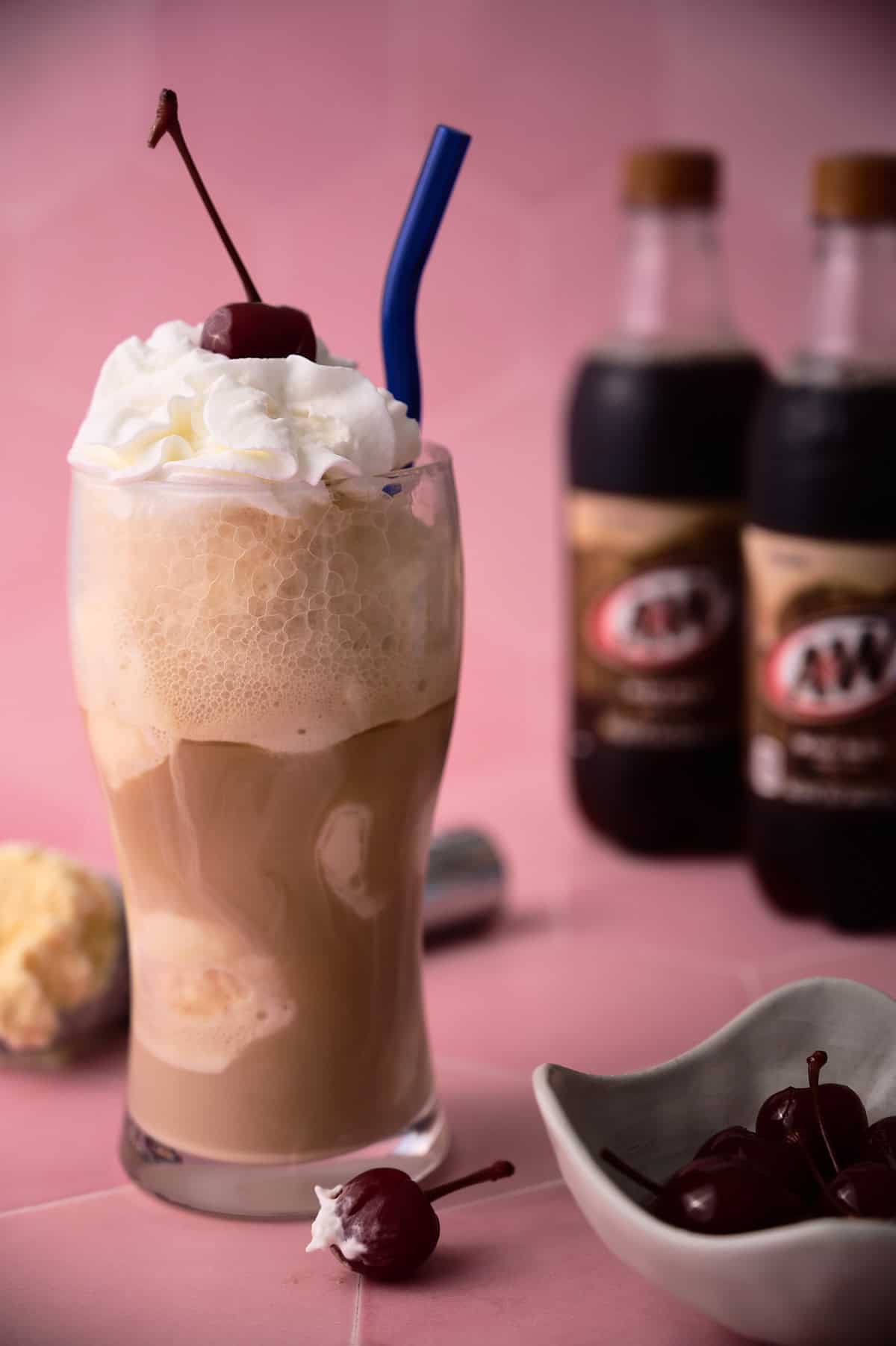 A blue straw is in a large glass with two bottles of soda behind it.
