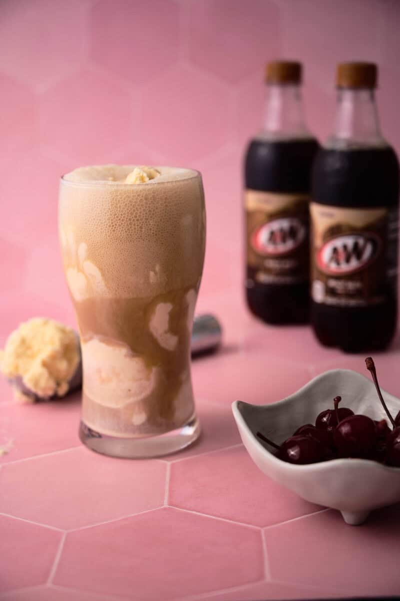 The root beer is fizzing in the glass with a bowl of cherries next to the glass.