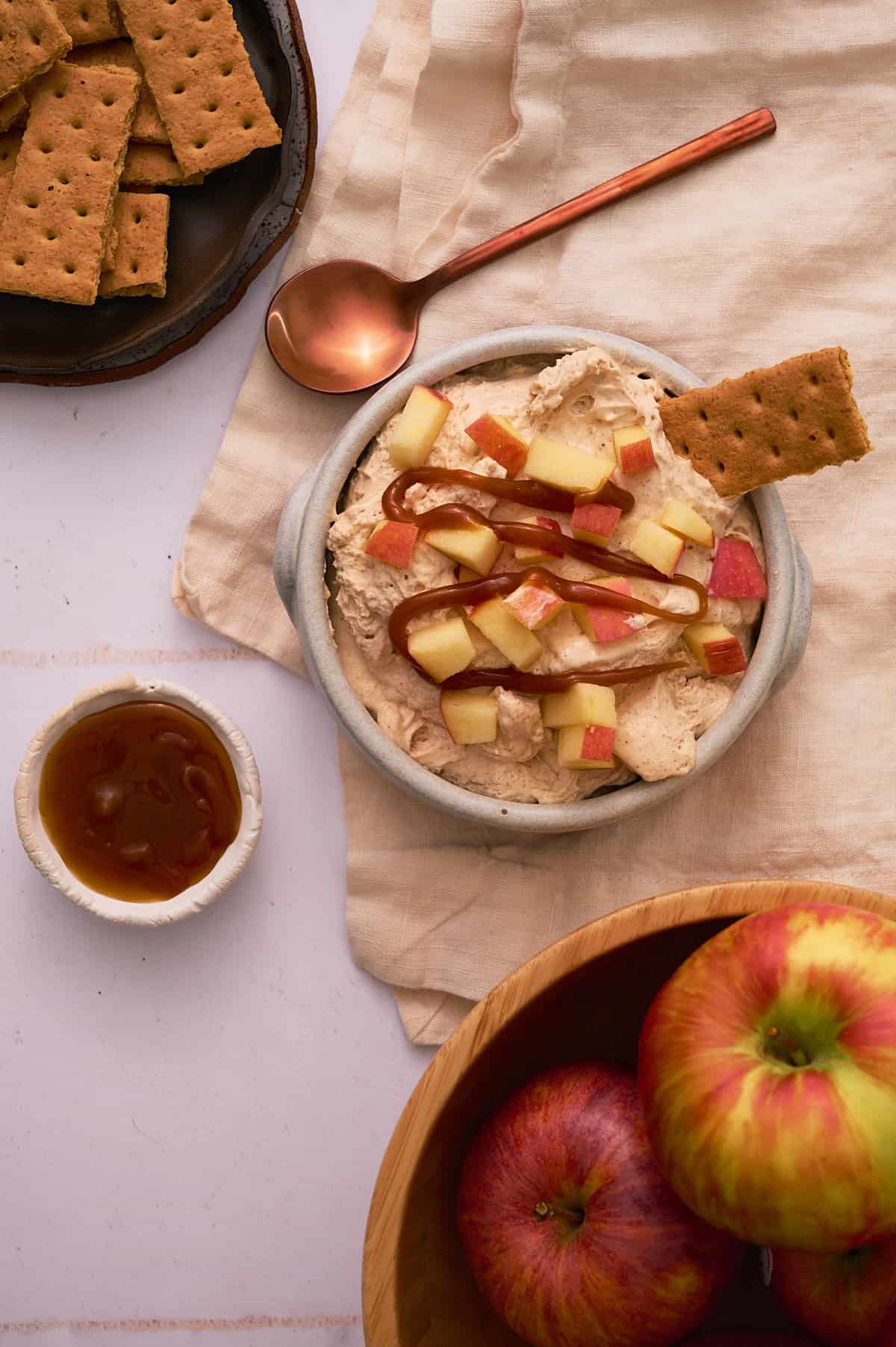 A bowl of the dip is surrounded by apples in a bowl.