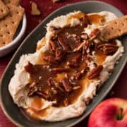 The pecan pie dip is in an oval plate with a whole apple next to it.