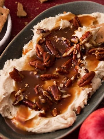 The pecan pie dip is in an oval plate with a whole apple next to it.