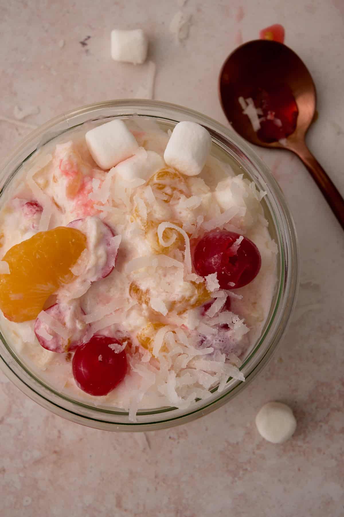 The marshmallows and cherries are topping the dish of ambrosia.