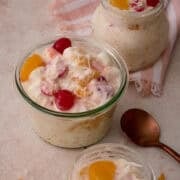 A golden spoon is next to a dish of the ambrosia topped with cherries.