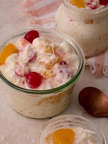 A golden spoon is next to a dish of the ambrosia topped with cherries.