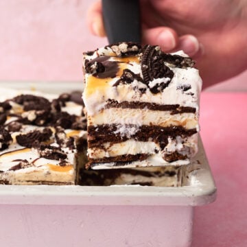 A slice of the ice cream sandwich cake is being taken out of the pan with a hand.