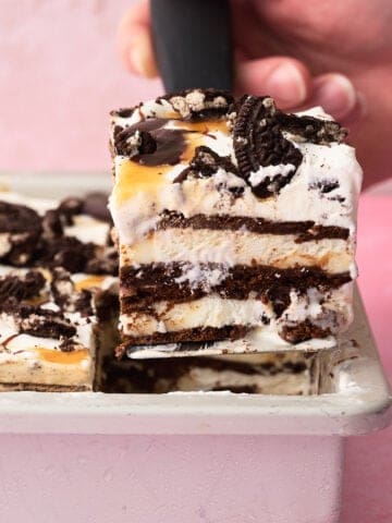 A slice of the ice cream sandwich cake is being taken out of the pan with a hand.