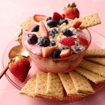 The cheesecake fruit salad is in a bowl with a graham cracker coming out of it.