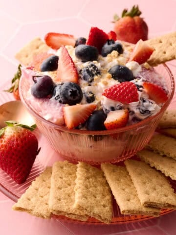 The cheesecake fruit salad is in a bowl with a graham cracker coming out of it.