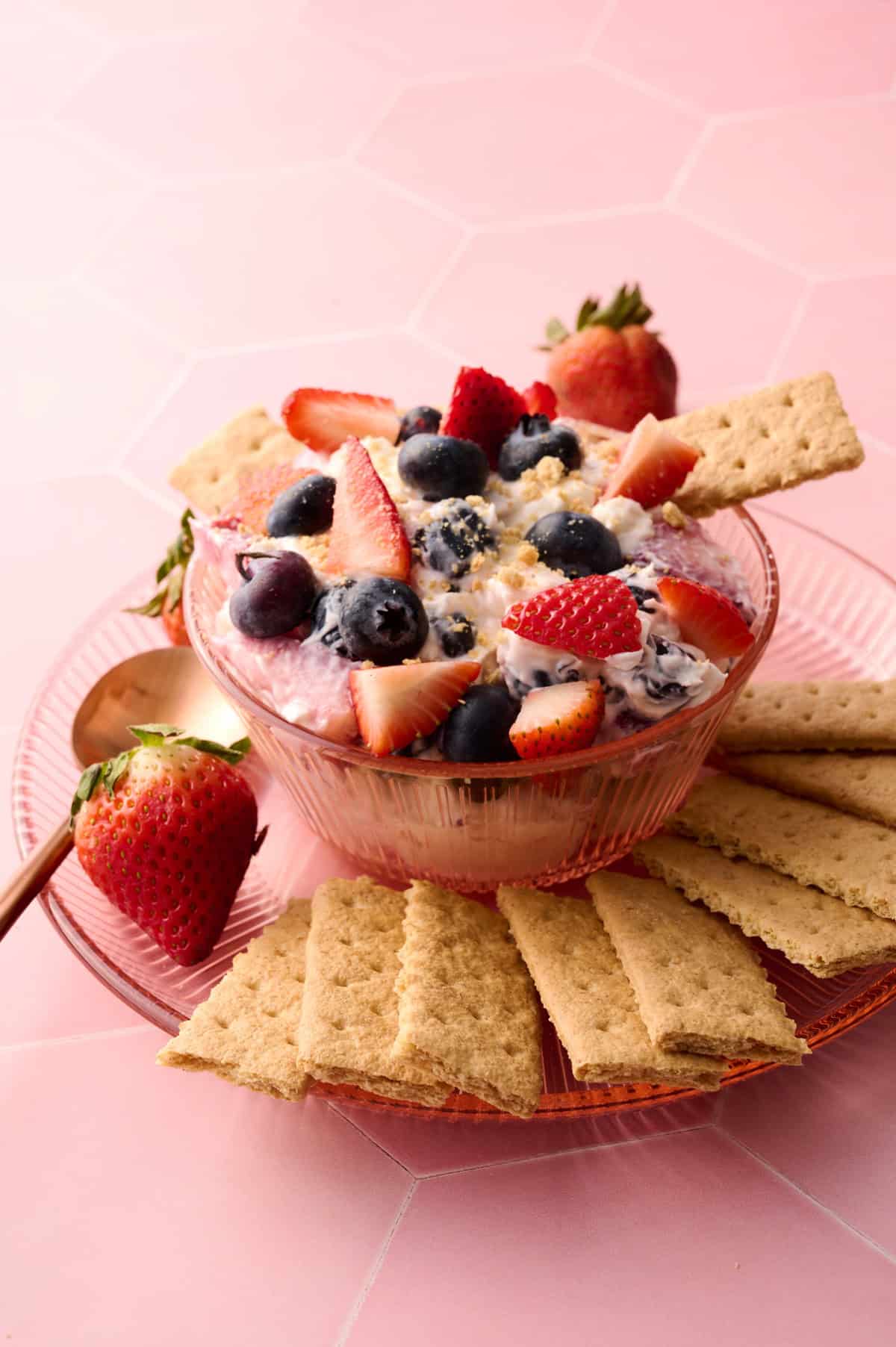 A graham cracker is sticking out of the bowl with the cheesecake fruit salad on it.