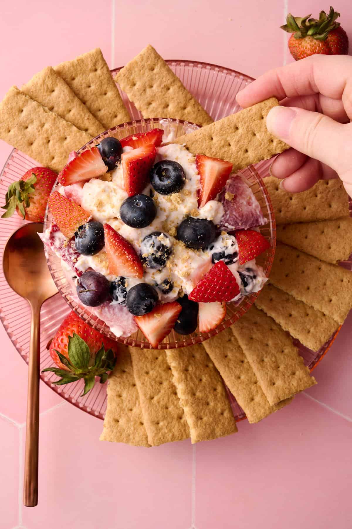 A hand is taking the cheesecake fruit salad out of the bowl.