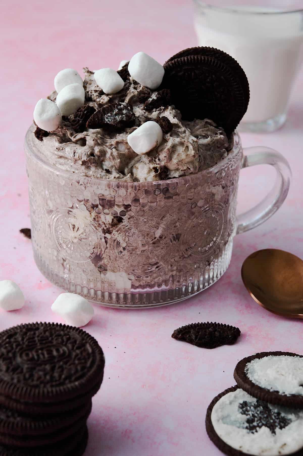 The oreo fluff is in a glass cup surrounded by oreos and pieces of oreos.