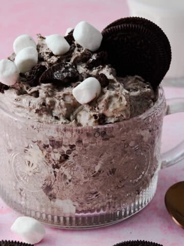 The oreo fluff is in a glass mug topped with marshmallows and oreos.